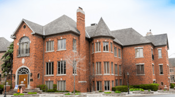 Exterior view of a large brick building with multiple windows and a grey sloped roof.