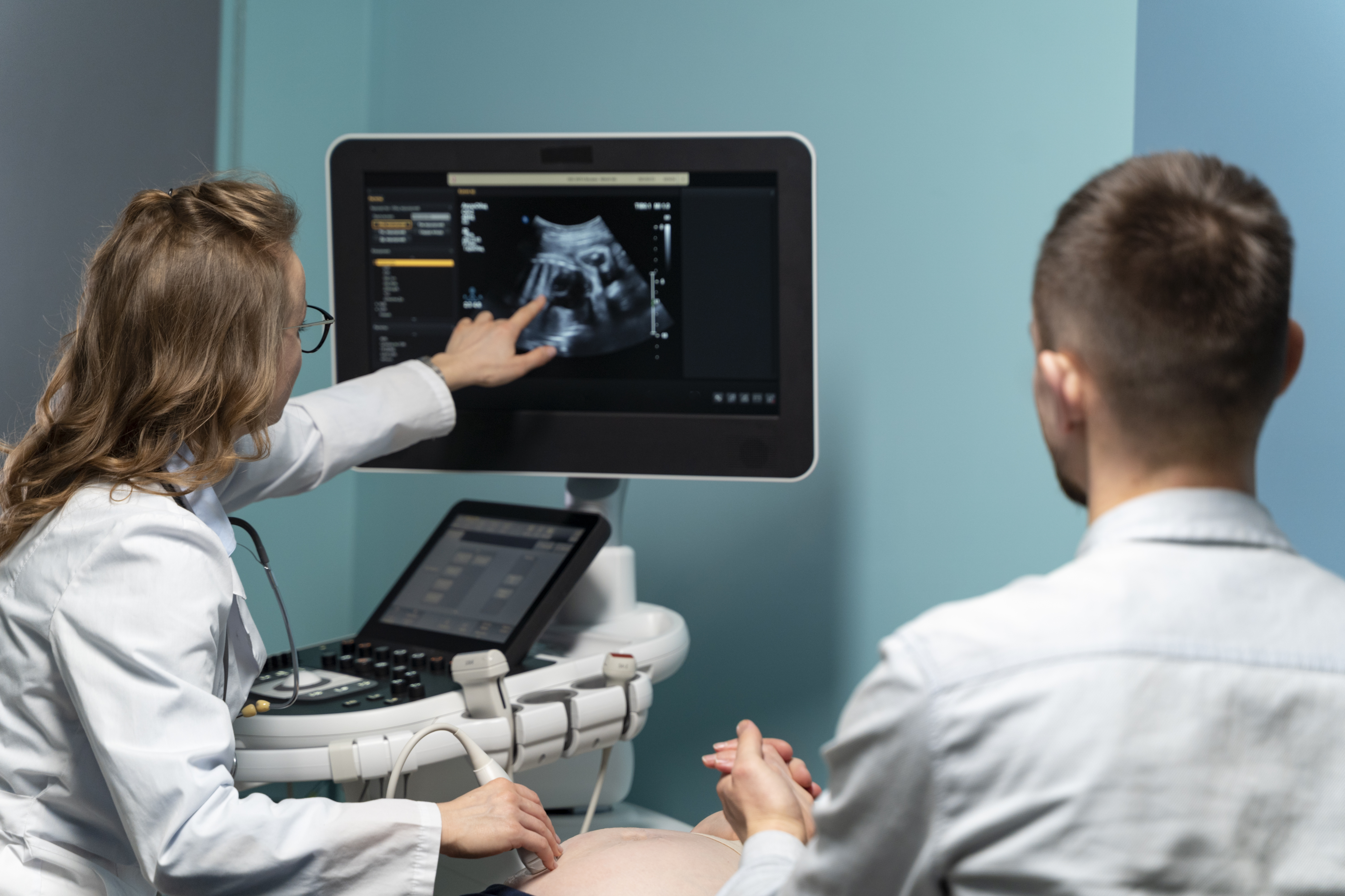 A healthcare professional demonstrating an ultrasound scan on a monitor to a patient in a clinical setting.